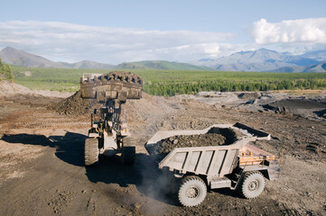 Loading of mountain soil into the body of a mining dump truck using a wheel loader, and further transportation of the cargo. Extraction of minerals in the mountainous region of Eastern Siberia © Letopisec