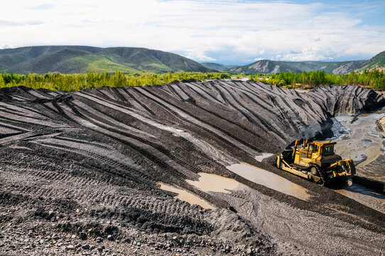 The bulldozer harrows the mountain soil, and then removes the top layer with an industrial bucket. Extraction of minerals in mountainous areas, in Siberia (gold mining)