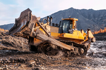 Bulldozer in the process of working in a mountainous wooded area in the autumn