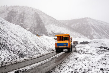 A mining dump truck drives on a dirt road in a mountainous area. It's still autumn, but already there is a snow cover around