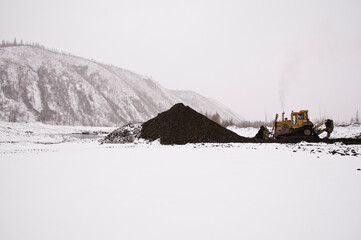 A bulldozer in a mountainous area in an industrial area shovels up a pile of mountain soil. Mining.