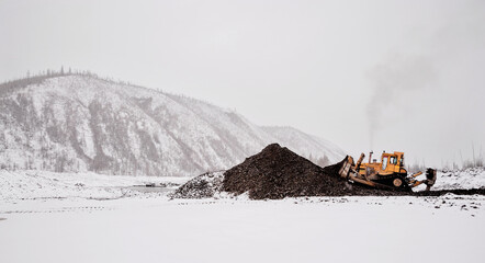 A bulldozer in a mountainous area in an industrial area shovels up a pile of mountain soil. Mining.