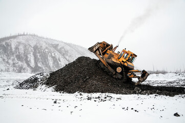 A bulldozer in a mountainous area in an industrial area shovels up a pile of mountain soil. Mining.