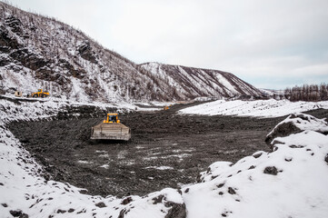 The bulldozer harrows the mountain soil, and then removes the top layer with an industrial bucket. Extraction of minerals in mountainous areas, in Siberia (gold mining)