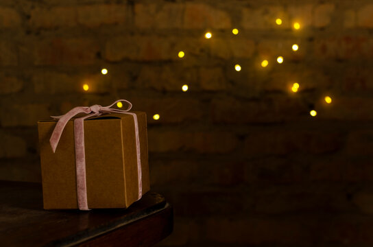 Brown Wrapped Gift Box On The Wooden Chair Against Bright Lights Bokeh On The Wall.Empty Space