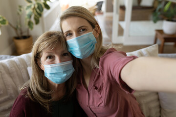 Senior woman and her daughter wearing face mask taking selfie at home