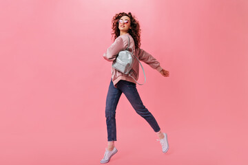 Pretty girl with curly hair holding backpack and moving on pink background