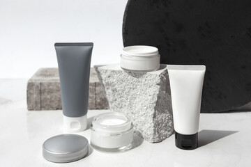 Mock up. Jars, tubes of cream or body lotion, white and gray, on pieces of stone on a white background with leaves. Natural eco organic cosmetics. Treatment spa beauty skincare. Healthcare, medicine