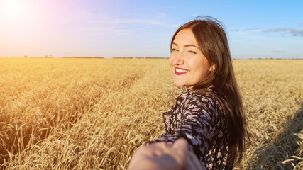 Brunette woman leads across a field of ripe wheat turning smiling. follow me concept