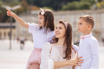 Obraz premium Young cheerful mom with kids on a walk in european city. Kids smiling and having fun. Summer portrait with space for text.