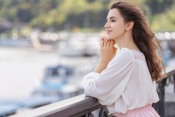 Young woman in romantic outfit outside on european streets near river. She relaxing alone under summer sun. Space for text.