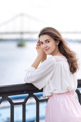 Obraz premium Young woman in romantic outfit outside on european streets near river. She relaxing alone under summer sun. Space for text.