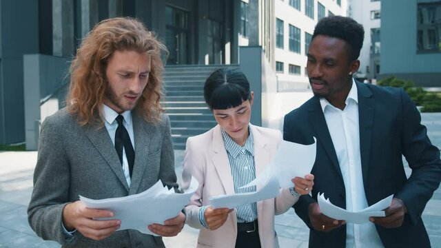 Smart diverse men and woman reading financial papers problem solving negotiating learing documents on office break outdoor. Corporate colleagues. Cooperation.