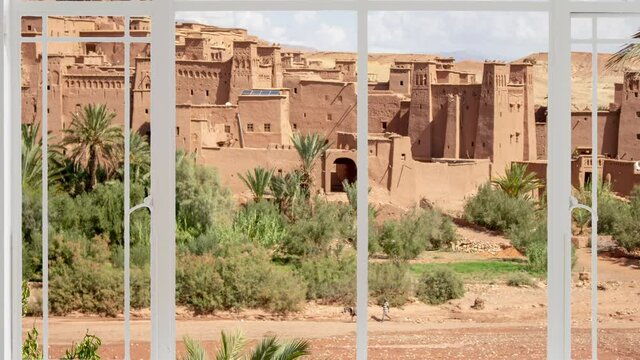 Ait Ben Haddou cityscape as seen from a white window while birds are flying. It is seen Kasbah near Ouarzazate in the Atlas Mountains of Morocco. UNESCO World Heritage Site since 1987. The red village