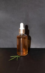 Glass bottle and dropper CBD OIL, THC tincture and cannabis leafs on black background. Laboratory Production of cosmetics with CBD oil. THC tincture