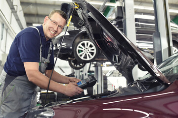 smiling car mechanic in a workshop - engine repair and diagnosis on a vehicle