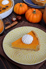 pumpkin pie with cinnamon and cream in a cut. Autumn table setting for Thanksgiving and Halloween. pumpkins, cinnamon sticks, plates, wooden background