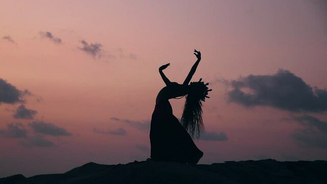 Silhouette of sexy, elegant and erotic arabian dancer performing belly dance moves on the beach during golden hour. Static. Slow motion.