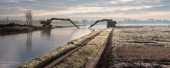 Dredging of an inland canal by cranes in winter at sunset. 
