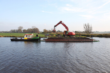 Dike improvement: push boat with a barge of clay being unloaded, in a traditional Dutch polder...
