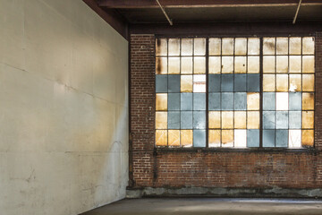 Corner of empty and abandoned factory floor with frosted windows and brick wall