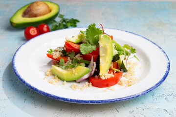 salad with avocado, tomatoes and herbs in a plate on a gray background