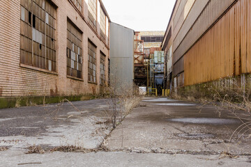 Fototapeta premium Low angle shot looking up between buildings at an abandoned factory site with grey sky