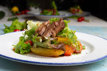 salad with beef, baked potatoes, tomatoes and herbs in a plate