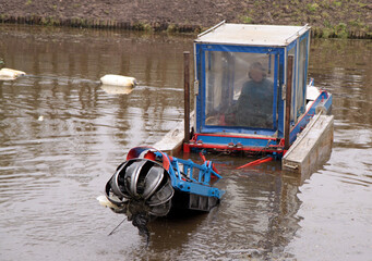 Small floating suction cutter dredger, its cutting head lifted above water for inspection.
