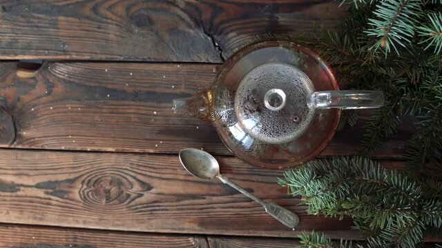 Christmas wooden background with a teapot of hot tea and fir branches. Tea leaves floating in the teapot