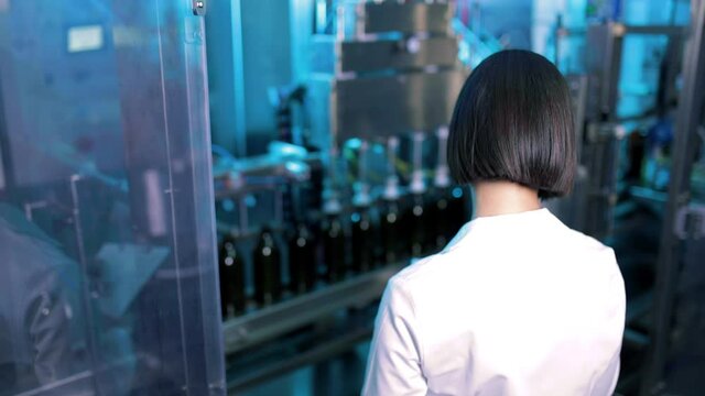 Ragazza chimico del controllo qualit&agrave; sta guardando la produzione di bottiglie nella fabbrica