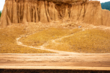 An empty wooden table with mountain views and a yellow sand floor with a trace of flowing water in the background.