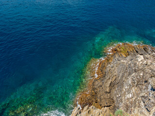 Aerial top view of turquoise sea waves hitting rocks. Amazing rock cliff seascape in the Italian coastline. Drone photography