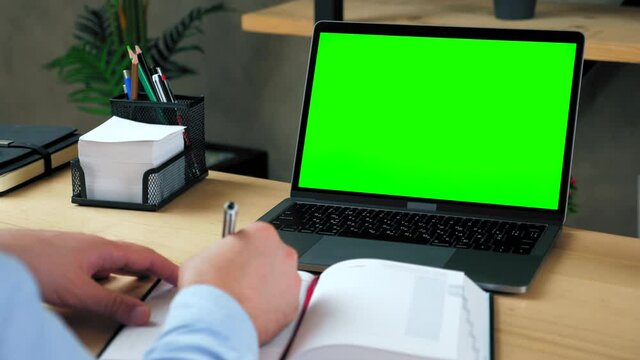 Green screen laptop computer concept: online remote distance learning education by web cam video call conference. Man student at home office sits table study writes information with pen in notebook