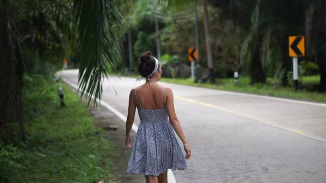 Beautiful girl walking along the palm road and hitchhiking and dances