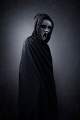 Fototapeta na wymiar Ghostly figure in hooded cloak in the dark