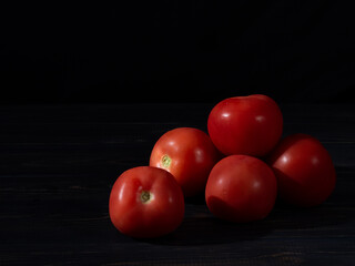 Whole red tomatoes and one sliced tomato on a dark wooden background. Close up.