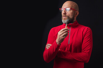 Bald man in his 40s with grey beard holding e-cigarette in his hand and ready to breath out the smoke. Male with slim body type, Dark black background. Addiction and bad habit concept - Powered by Adobe