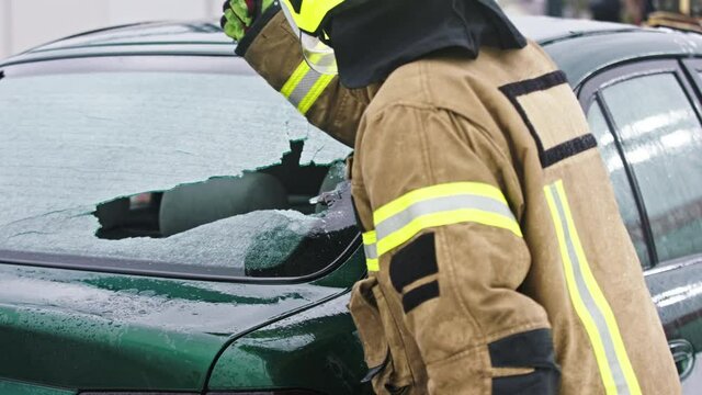 Firefighter beraking glass on car window extricate trapped victim from the car. High quality 4k footage