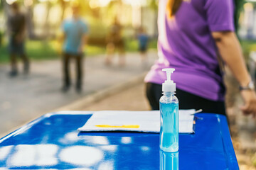 Blue alcohol gel bottle and a register book on the table for athletes to prevent Corona Virus (COVID -19) infection and spread before exercising in public park. New normal lifestyle. Selective focus