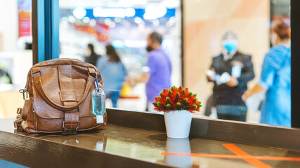 Mini portable alcohol gel bottle to kill Corona Virus(Covid-19) hang on a brown leather shoulder bag on counter in coffee shop.New normal lifestyle. Health care concept. Selective focus on alcohol gel