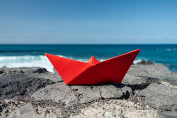 Fototapeta na wymiar Red paper boat in front of the ocean outdoors
