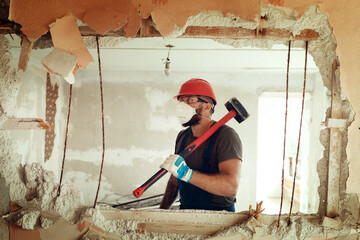 builder with a hammer in his hands breaks the cement wall The builder is dressed in a protective suit and helmet