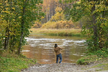 Fisherman using rod fly fishing in forest river at autumn