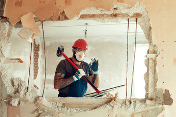 builder with a hammer in his hands breaks the cement wall The builder is dressed in a protective...