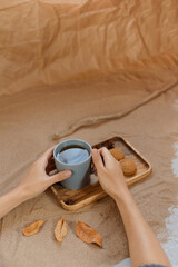 A mug of tea on a wooden tray, next to homemade cookies and spices. Background of sand and craft paper.
