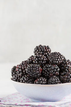 Bowl  with ripe blackberries on a delicate grey surface. Macro photo of ripe blackberries.