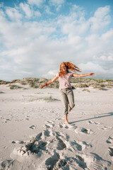 Junge Frau tanz mit fliegenden kupferfarbenen Haaren am Strand von Amrum