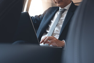 Businessman in suit working on laptop computer inside a car during going to office