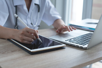 Doctor using stylus pen for prescription on digital tablet and working on laptop computer in...